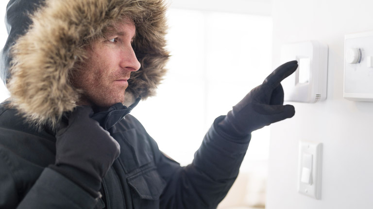 cold homeowner adjusting thermostat